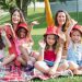 Two women and four girls enjoy a sunny picnic in Portugal, waving happily in the park.